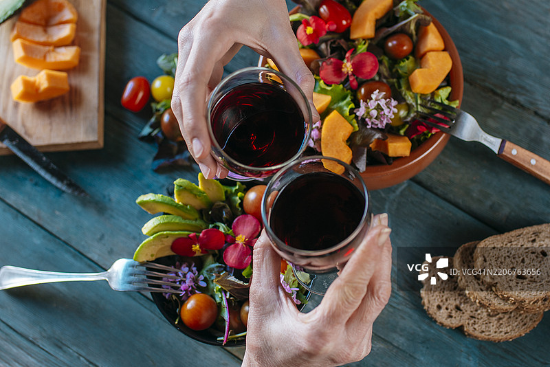 朋友们在乡村风格的桌子上举杯庆祝，享用红酒和可食用花卉沙拉图片素材