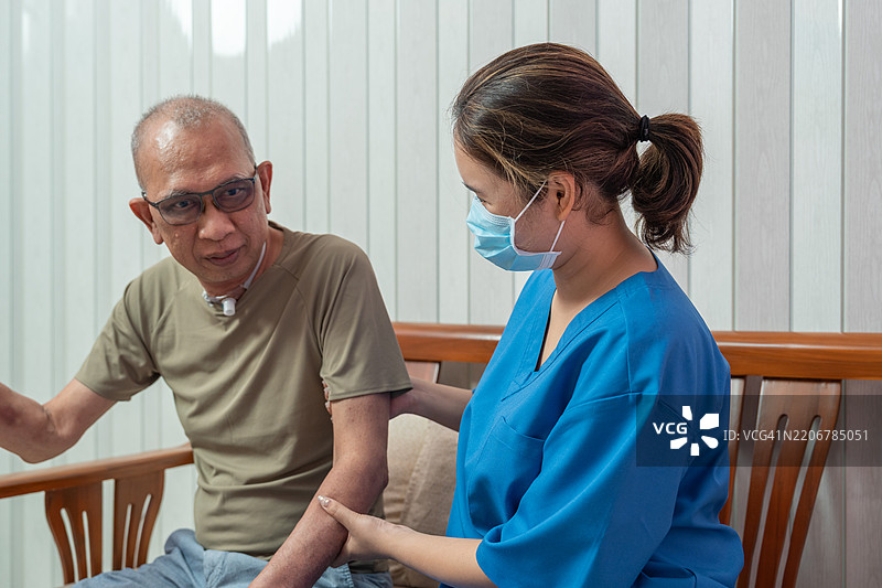 年轻的亚洲女性护士在家中或老年日托中心帮助一位亚洲老年男性站起来，护士愉快地照顾这位老年患者。图片素材