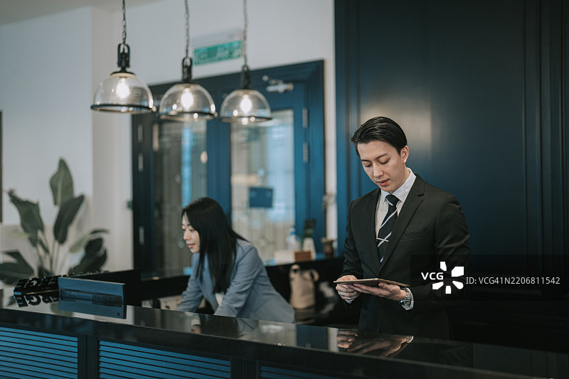 奢华酒店的亚洲华人礼宾经理/接待员在机场贵宾休息室工作，使用数字平板电脑检查酒店房间预订信息。图片素材