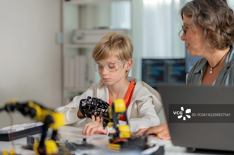 一位专注的学生认真观察她的科学老师讲解如何使用遥控器操作机械手臂。这种互动课堂体验融合了人工智能、编程和创新，激发了好奇心和技术能力。图片素材