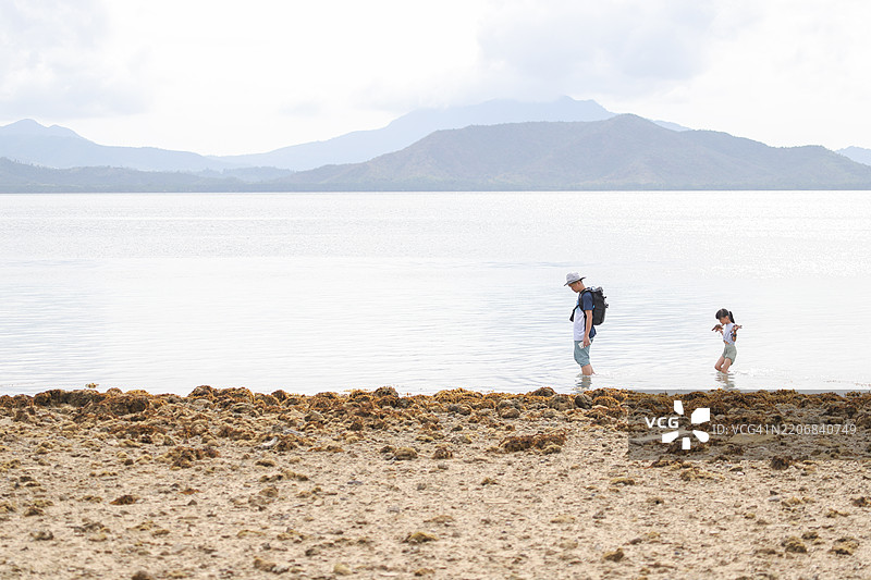 一位亚洲父亲和女儿在退潮时观察海洋生物。他们正在沙滩上散步。图片素材