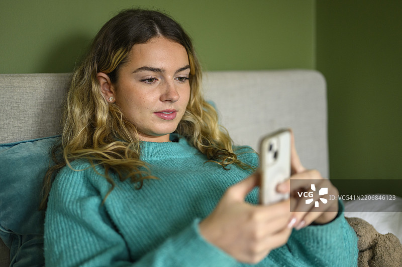 放松的19岁女性在家中使用智能手机图片素材