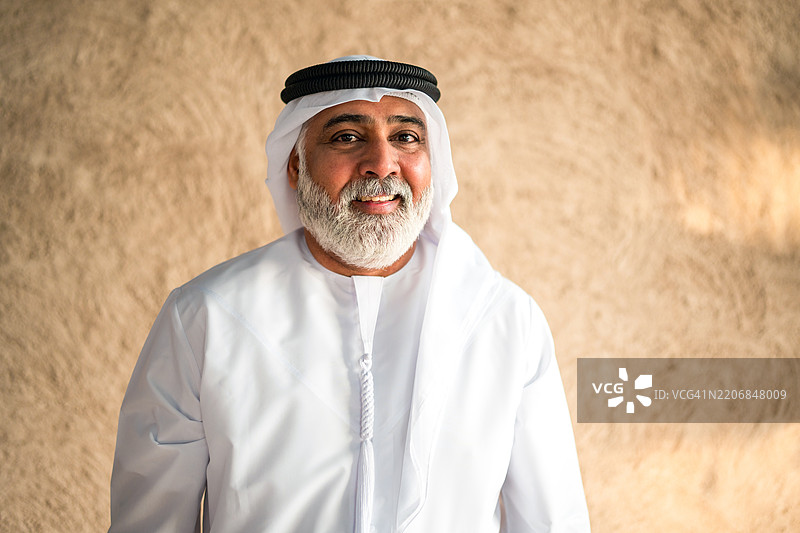 微笑的阿联酋老年男性穿着传统白色坎杜拉，背景为米色纹理图片素材