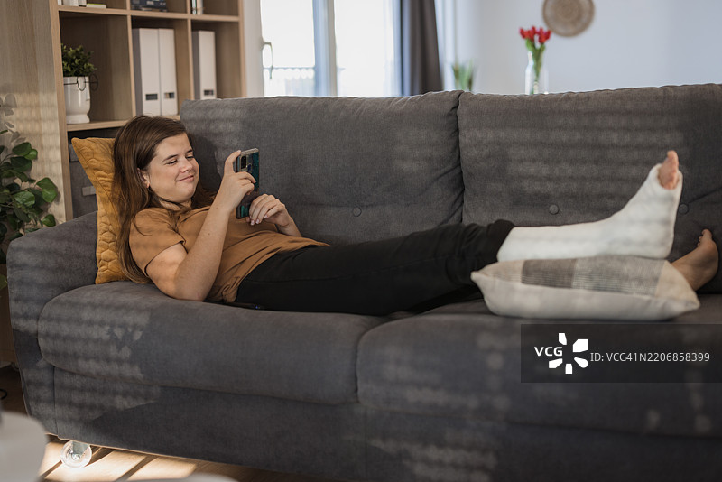 女孩微笑着休息，腿上打着石膏。图片素材