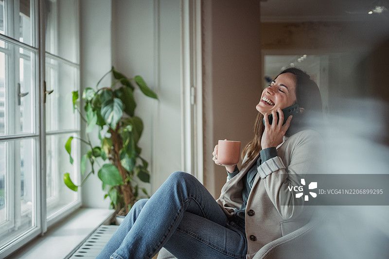快乐的女商人在窗边放松，喝着咖啡并打电话。图片素材