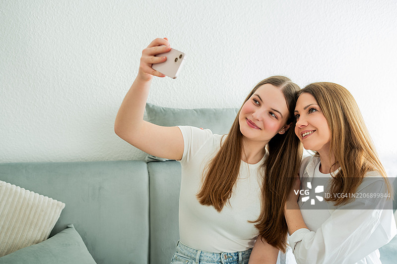 美丽的母亲拥抱着她的青春期女儿，两人一起看手机。孩子与母亲之间的情感关系。母亲节。节日问候。图片素材