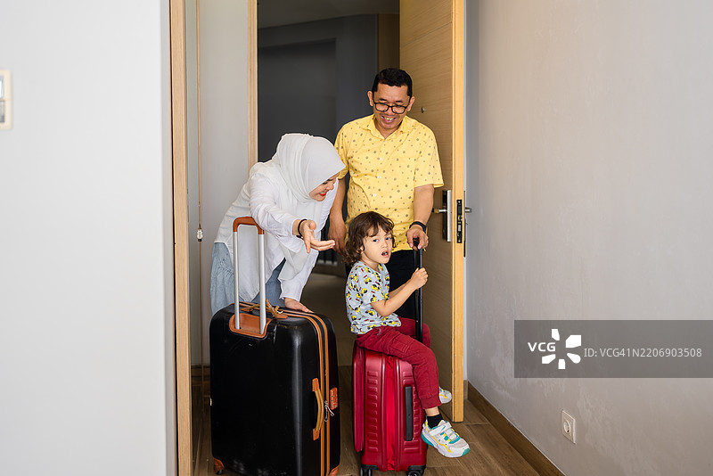 快乐的年轻家庭带着一个孩子走进豪华酒店的房间图片素材
