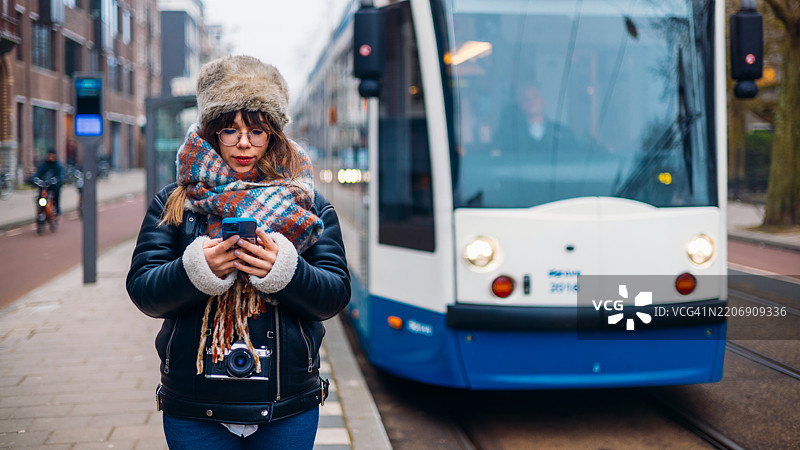 年轻女性在城市环境中靠近公共电车使用智能手机图片素材