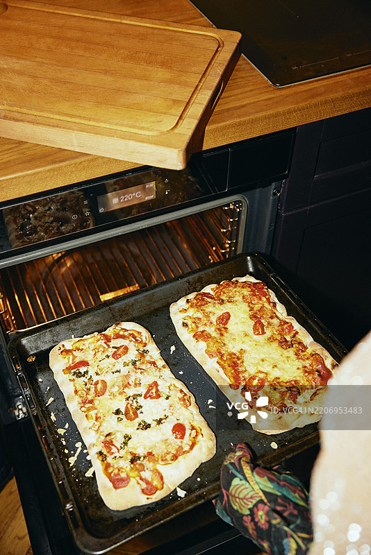 高角度视图下的人正在从烤箱中取出新鲜出炉的比萨饼图片素材