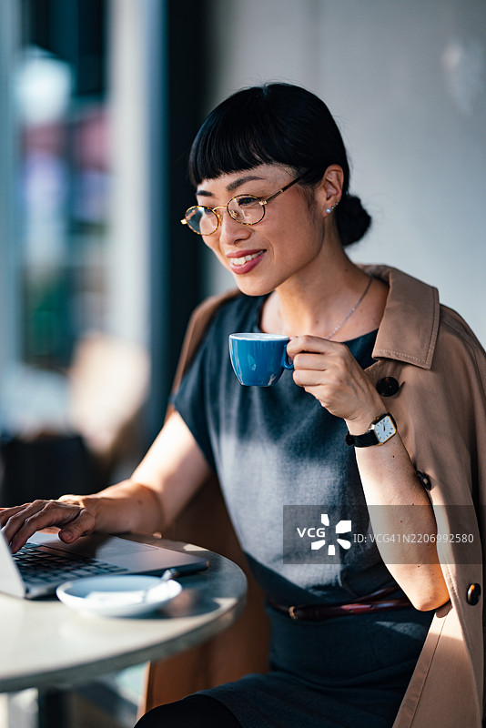 自信的女商人在咖啡馆享受咖啡并使用笔记本电脑工作图片素材