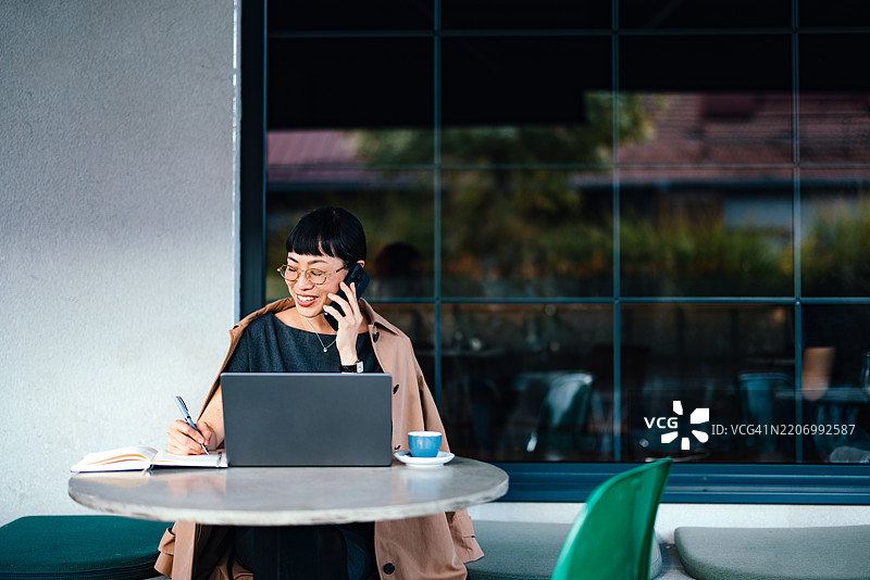 在户外使用笔记本电脑和手机，手边有笔记和咖啡的女商人图片素材