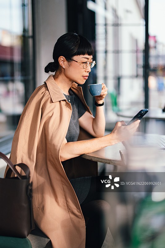 时尚的女商人在现代咖啡馆享受咖啡，手中拿着智能手机图片素材