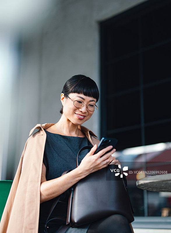 在户外环境中微笑的女商人查看手机图片素材