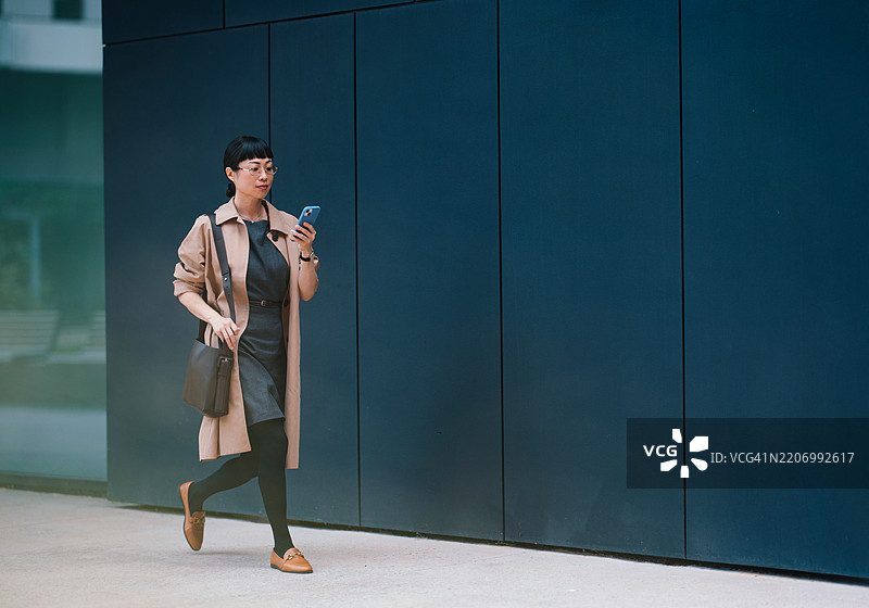 时尚的女商人在城市环境中走动，同时使用智能手机图片素材