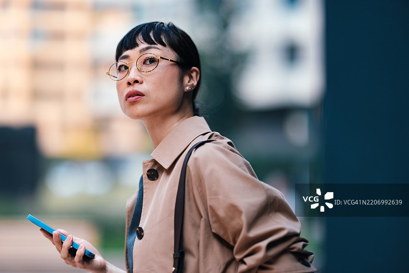 自信的女商人在城市中走着，手里拿着智能手机图片素材