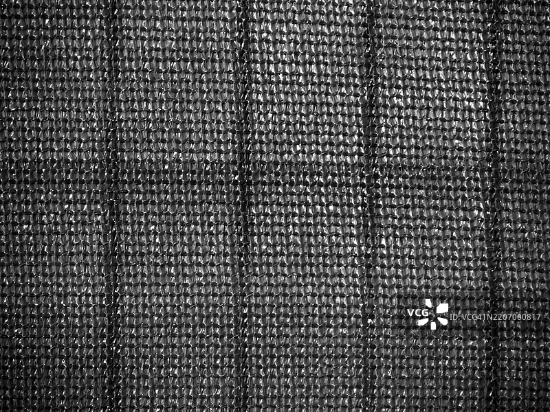 背光下编织塑料防水布的网状特写，粗糙的纹理。黑白色。图片素材