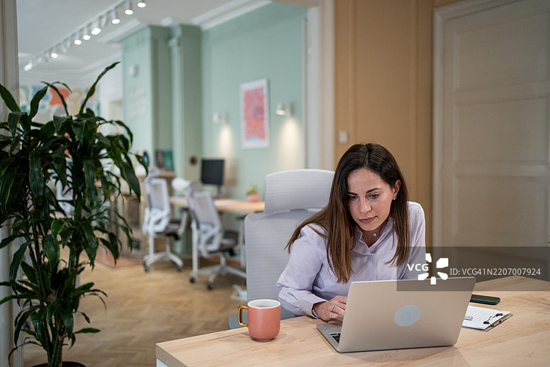 专注的女商人在现代办公室使用笔记本电脑工作图片素材
