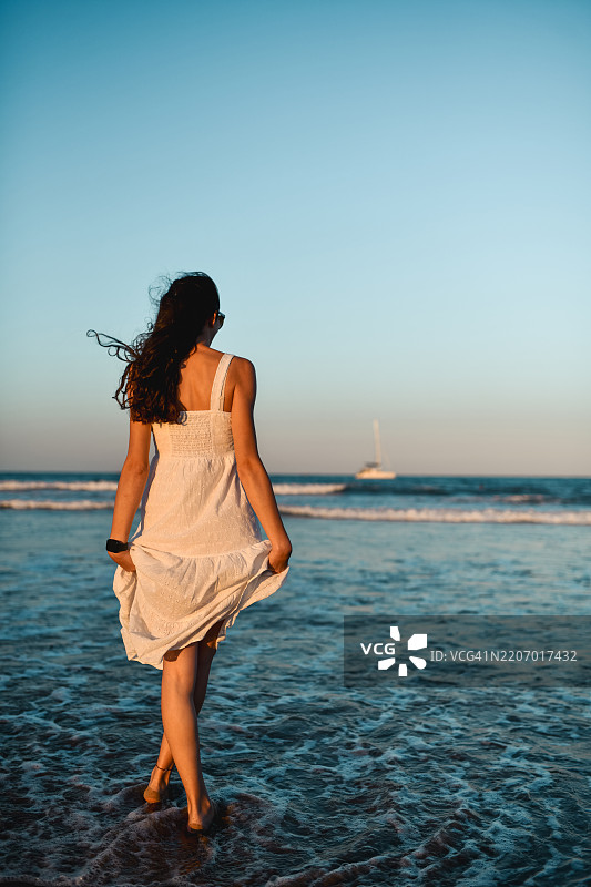 穿着夏季裙子的女性走向海边，欣赏海洋的美丽图片素材