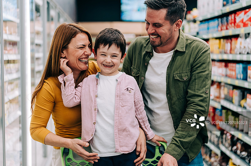 微笑的家庭在超市里推着购物车挑选商品。图片素材