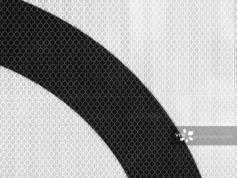 白色网格塑料背景上的弯曲黑线。交通标志反光表面的特写。图片素材