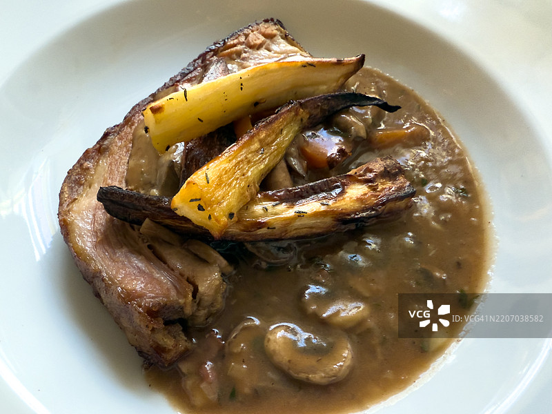 一盘慢烤五花肉配烤根菜。图片素材