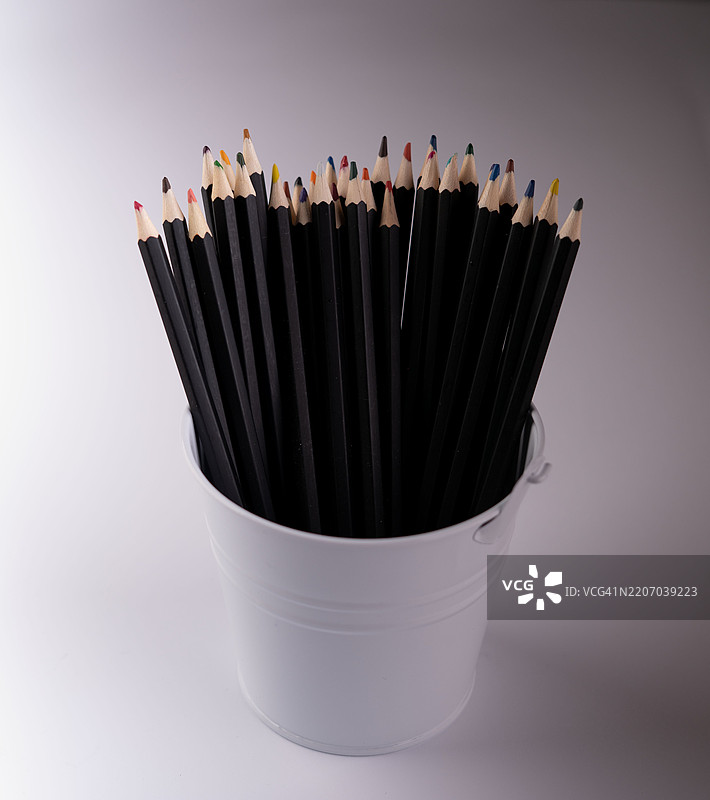 一组色彩鲜艳的彩色铅笔，放在一个时尚的白色笔筒中，展示了多种颜色，适用于创意艺术和教育用途的绘画和素描项目。图片素材