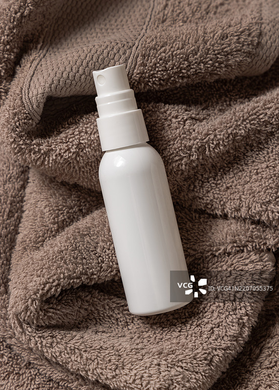 白色空喷雾奶油瓶放在棕色浴巾上，俯视图，自然草本化妆品的样机图片素材