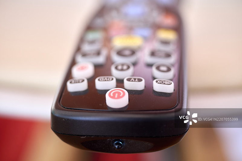 特写镜头展示带有发光电源按钮的遥控器，突显电子切换和便捷设备管理，实现即时娱乐激活。图片素材