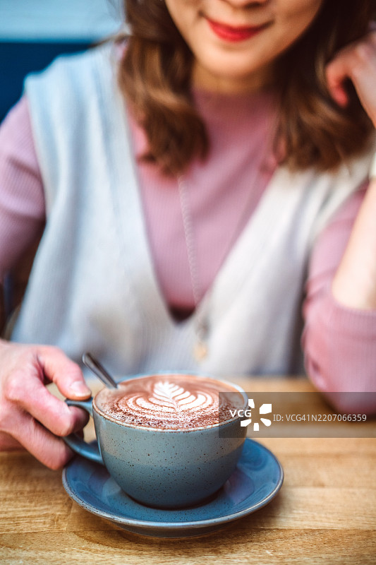 一位女性在舒适的户外咖啡馆享受带拉花的咖啡图片素材