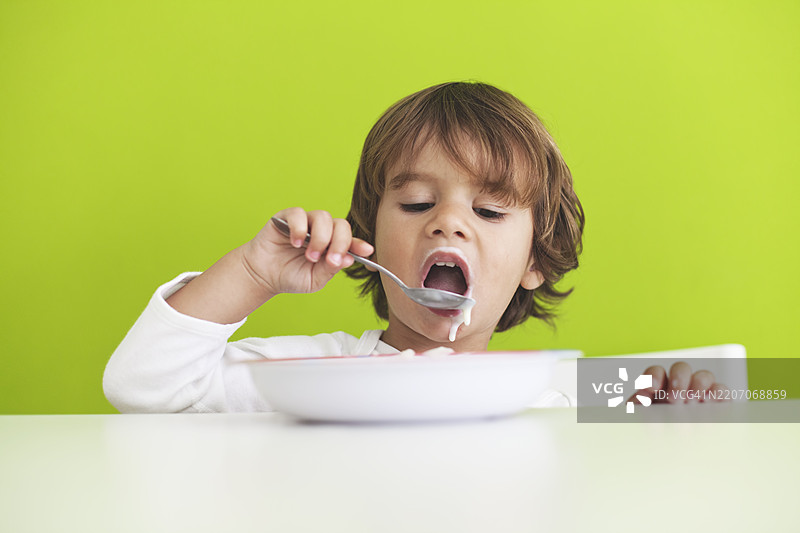 孩子在明亮的绿色背景下的桌子上享受酸奶图片素材