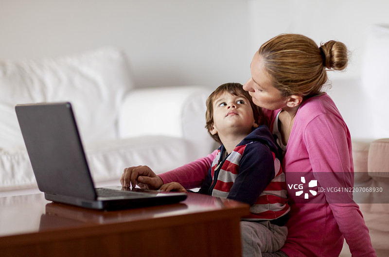 母亲和儿子在家中一起使用笔记本电脑，共享温馨时刻图片素材