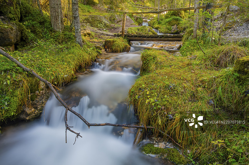 一座木桥横跨急流的景观，长时间曝光，意大利南蒂罗尔的多洛米蒂，普兹-盖斯勒自然公园，圣玛德琳娜，富内斯，维尔诺斯谷，欧洲图片素材