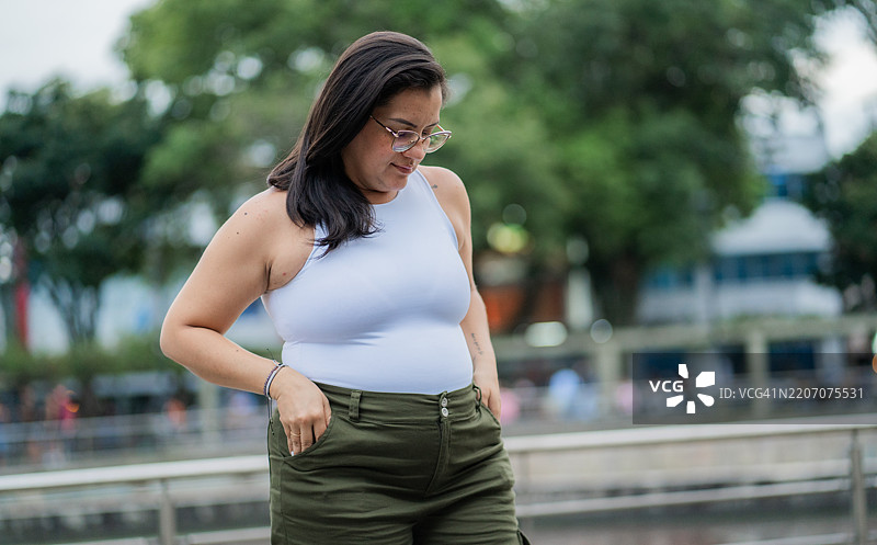 年轻孕妇在公园里站着，侧身看向地面，沉思中。图片素材