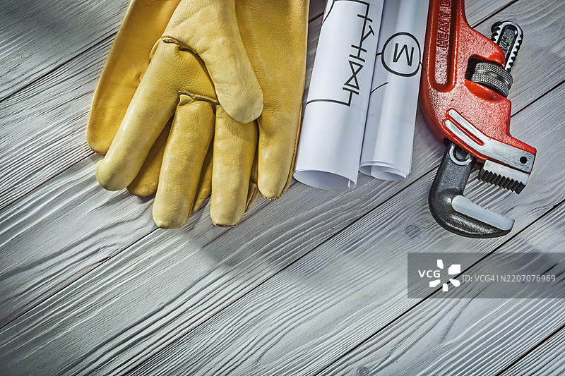 管道工程卷制管道蓝图、管钳、黄色皮革工作手套，背景为复古白色木材。图片素材