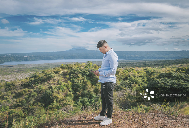 年轻男子在自然环绕的观景点使用手机。此人正在美丽的风景观景点马萨亚使用手机。图片素材
