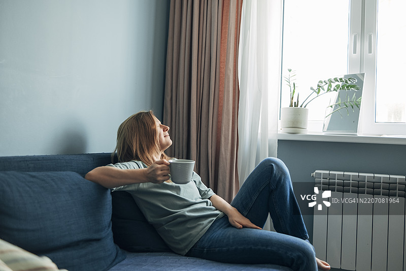 女人在家沙发上闭眼休息，手里拿着一杯咖啡，正在进行数字排毒，远离电子设备。图片素材