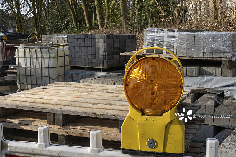 橙色旋转警示灯在建筑工地上发出危险信号，周围有木托盘、混凝土砖和IBC水箱，地点：德国北莱茵-威斯特法伦州博特罗普，欧洲图片素材
