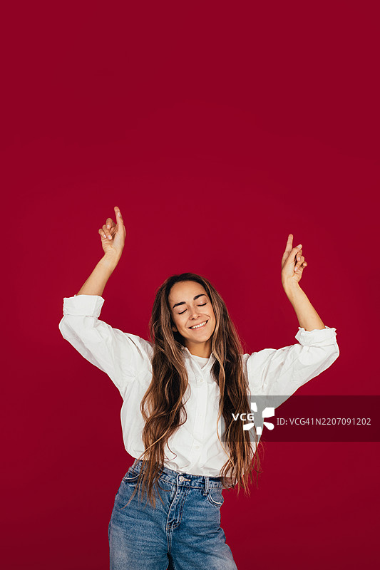 快乐的女性在鲜艳的红色背景前摆姿势，面带愉悦的表情图片素材