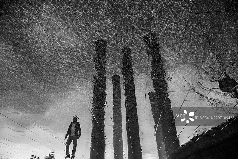 一个人在湿地面上的倒影和黑色柱子图片素材