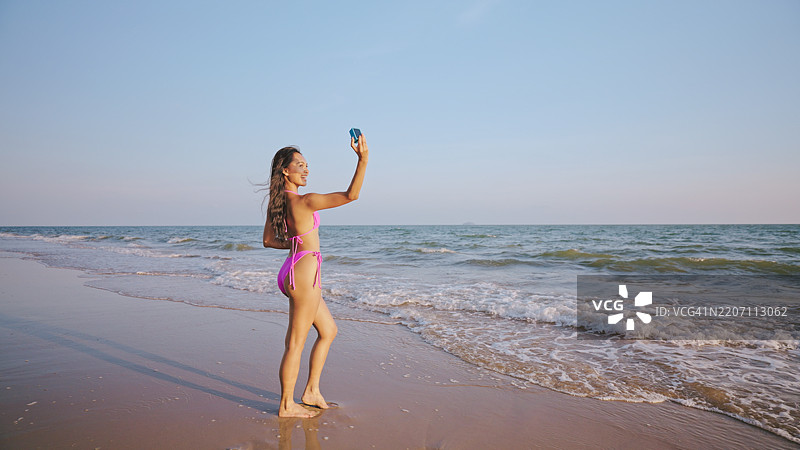 快乐的女人在阳光明媚的海滩上自拍。图片素材