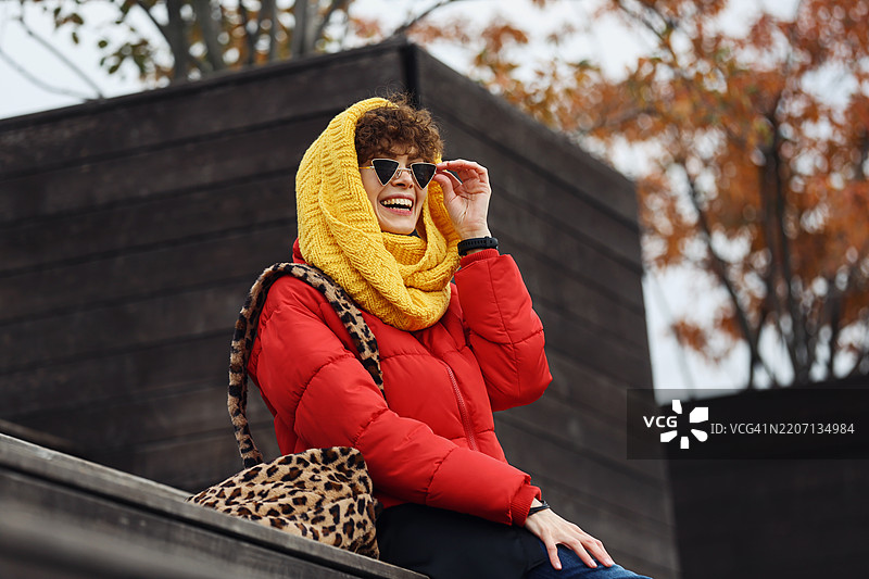 年轻自信的女性穿着黄色针织围巾，坐在木质街头露台上，微笑并大笑。图片素材