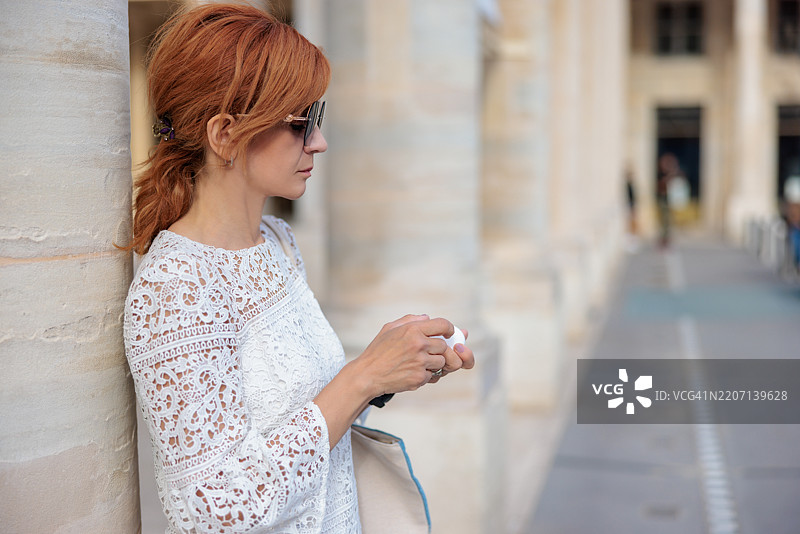 美丽的女性站在柱廊旁，取出耳机为智能手表，正在巴黎出差。图片素材