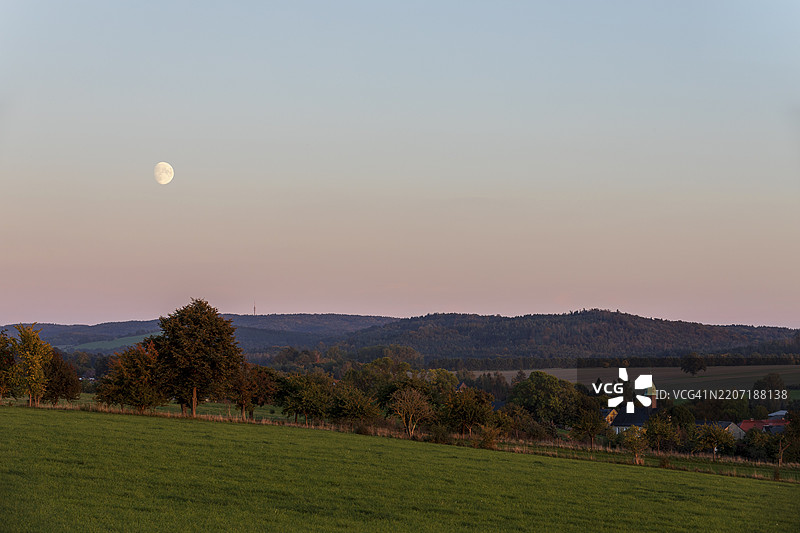 傍晚的氛围，月亮照耀下的上卢萨蒂亚高地和斯托尔彭的朗根沃尔姆斯多夫村教堂，德国，欧洲图片素材