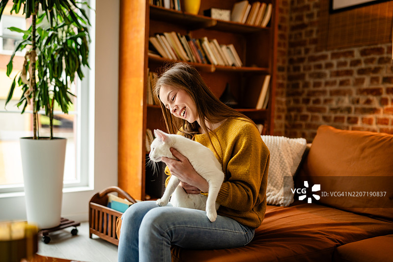 年轻女性在充满温暖和个性的明亮客厅里与她顽皮的猫咪享受温馨时刻图片素材