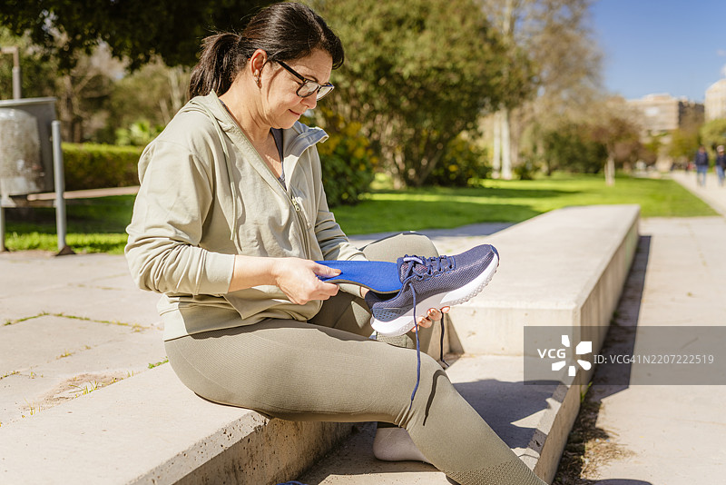 穿着运动服的女性正在跑鞋中放入鞋垫，为训练做准备。图片素材