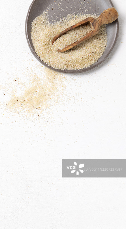 灰色盘子上的生未煮的丰年米种子，旁边有一个木勺，白色桌面俯视图，非洲谷物图片素材