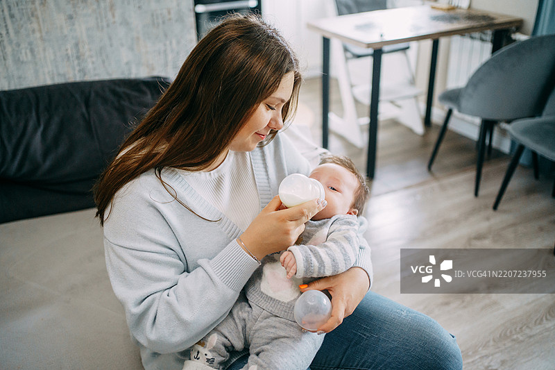 年轻母亲在家里给新生儿喂奶粉图片素材