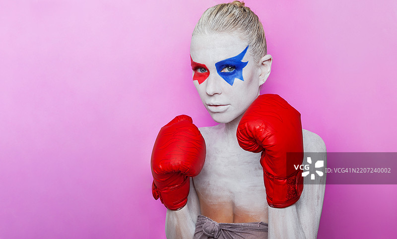 一位年轻女性的肖像，她的脸上有身体艺术，戴着红色拳击手套。图片素材