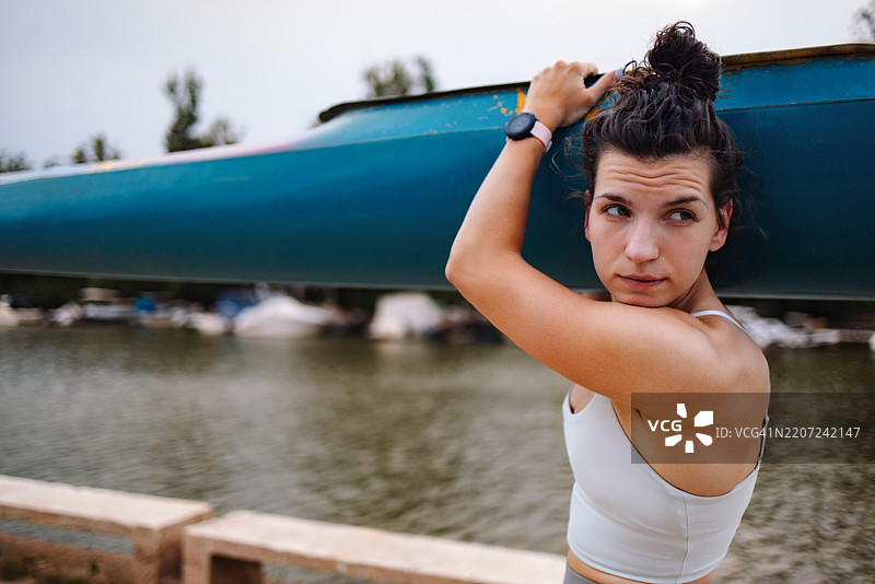 年轻女性在风景如画的河岸上搬运皮划艇图片素材