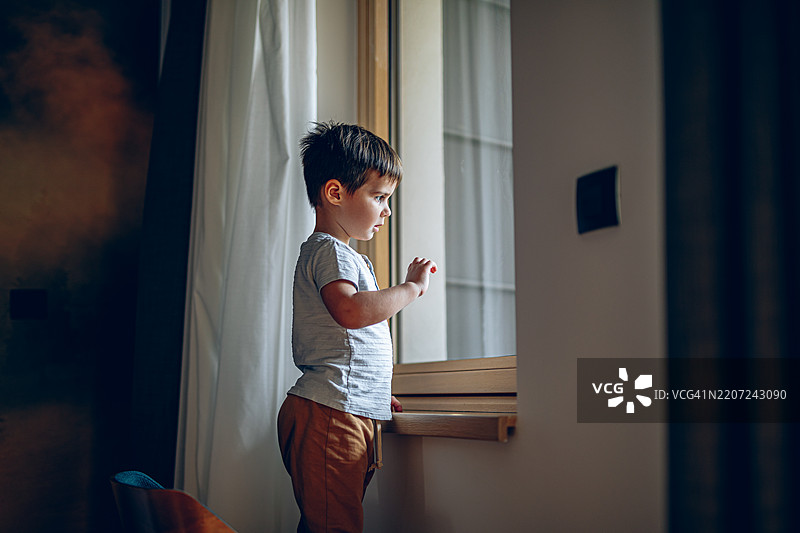 小男孩在家里透过窗户等待父母回家图片素材
